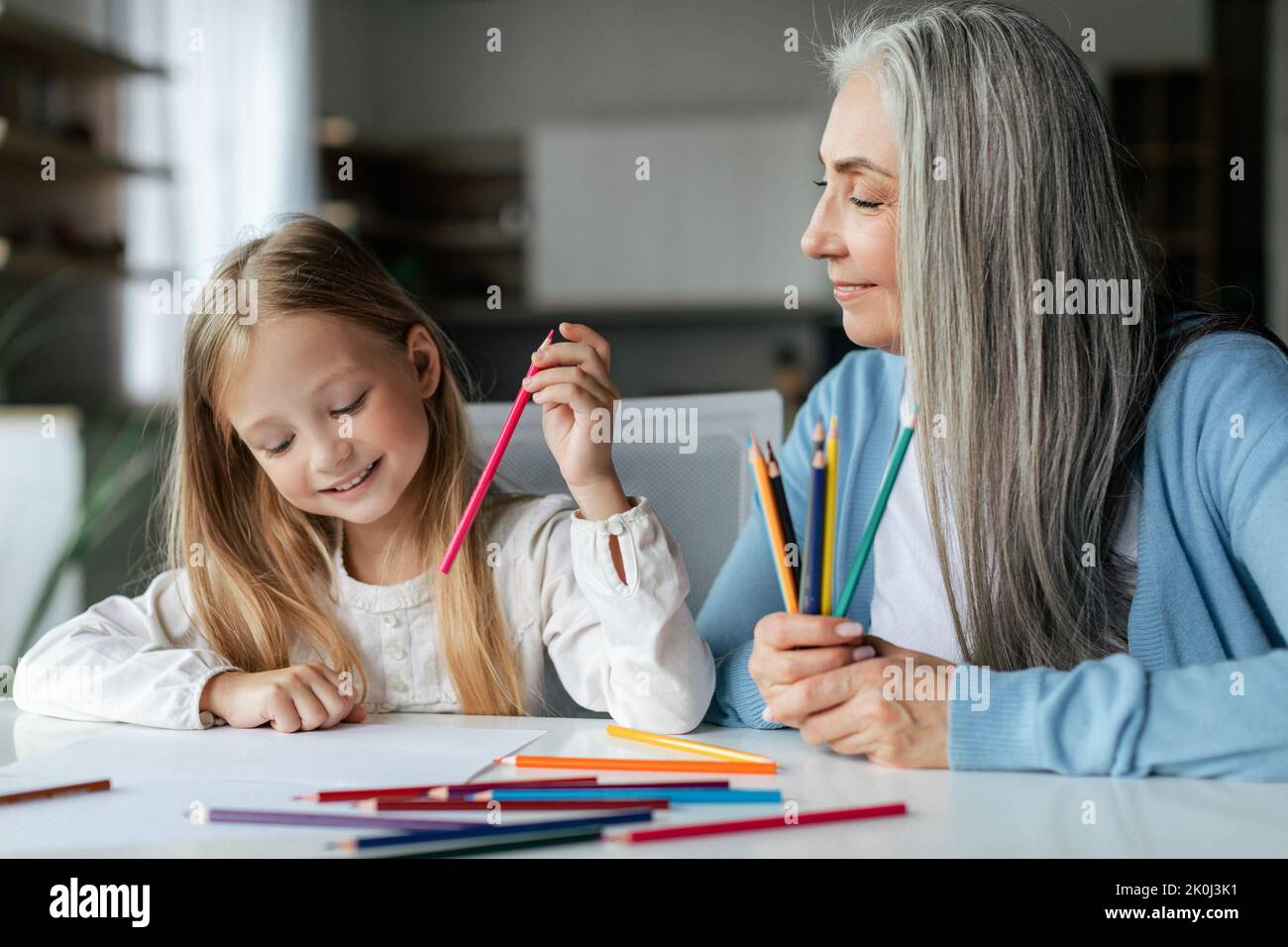 Happy caucasian little girl with elderly grandma with colorful pencils draw picture on table, enjoy study Stock Photo