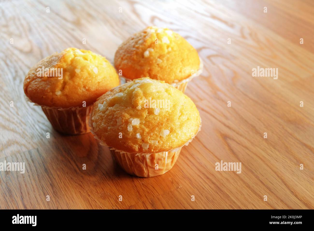Three lemon flavored sponge muffins with sugar crystals sprinkled on top. On a wooden table surface copy space Stock Photo