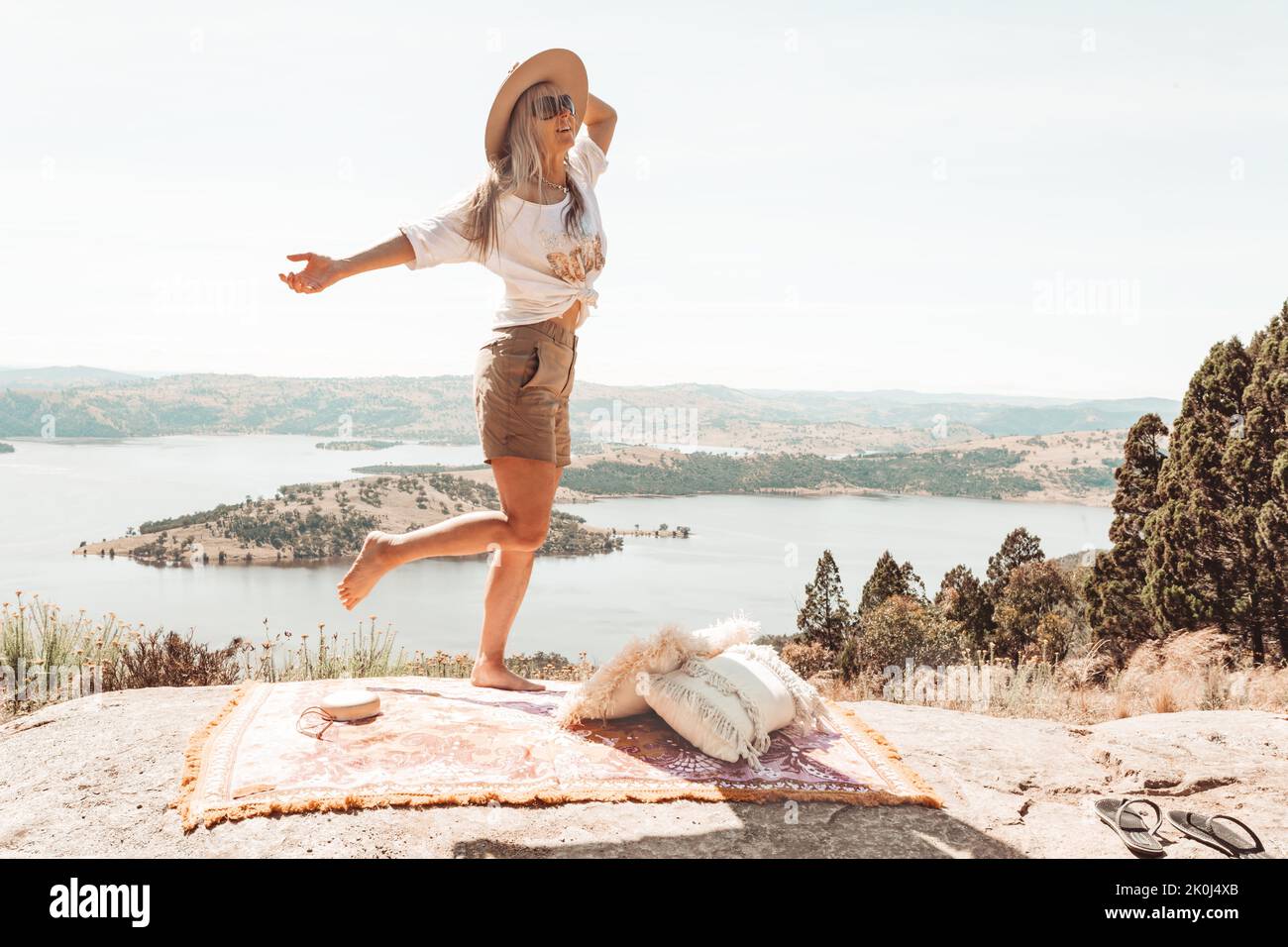Happy exuberant woman dancing high on a rocky outcrop with views over waterways Stock Photo