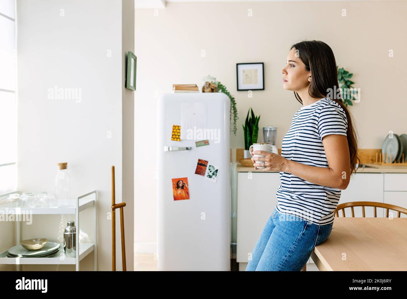 Thoughtful young adult woman drinking coffee on the kitchen in the morning Stock Photo