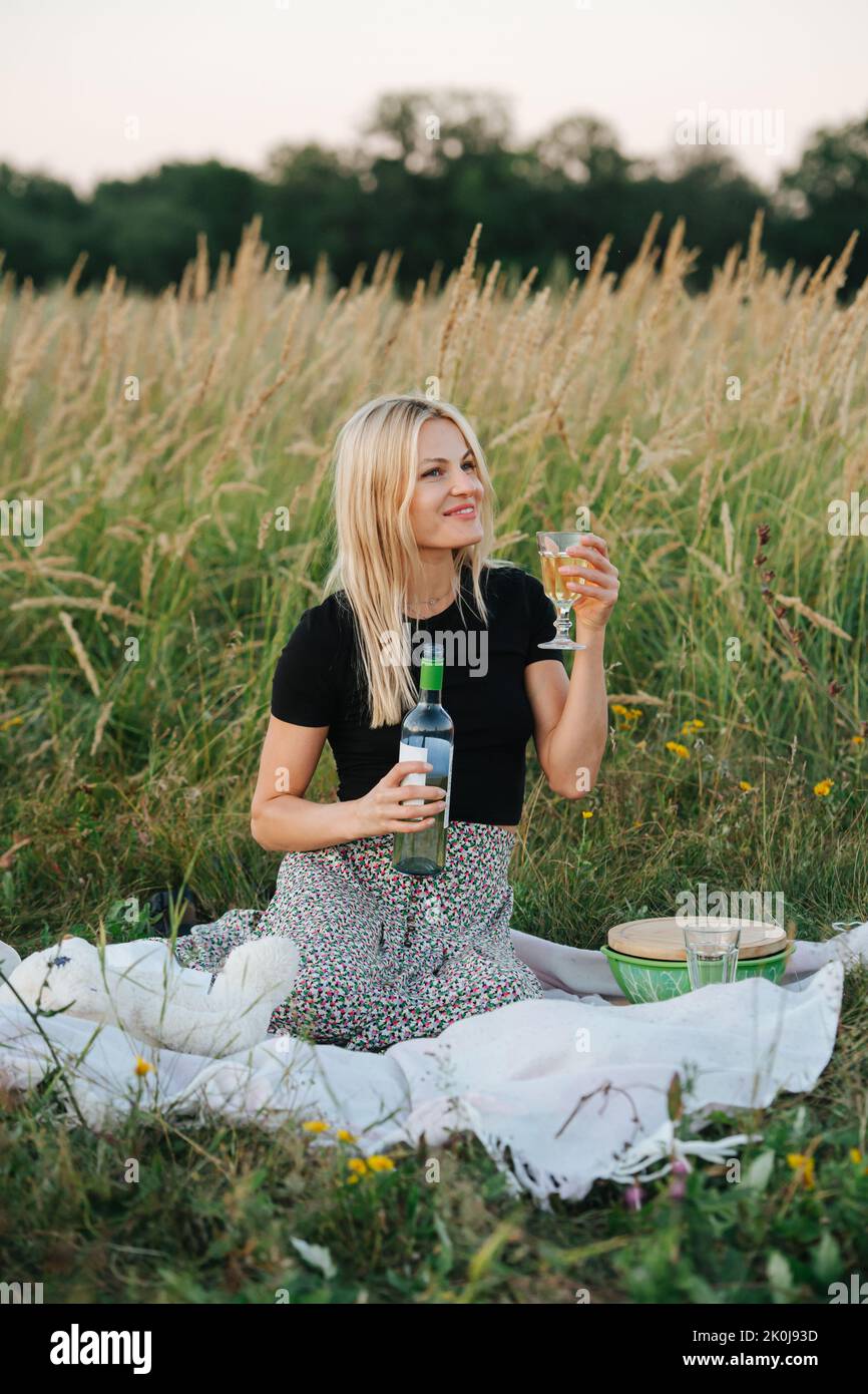 Joyful young blond woman in a field lifting a glass of a white wine Stock Photo