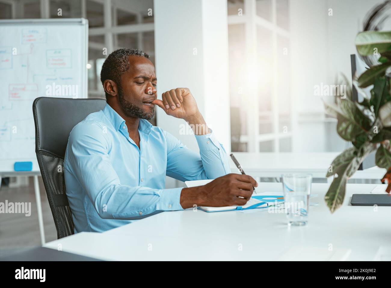 Confident African businessman taking notes while sitting in modern office Stock Photo