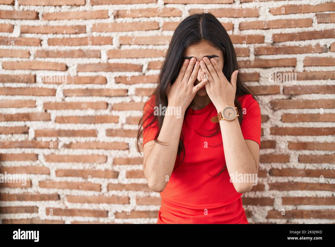 Young teenager girl standing over bricks wall rubbing eyes for fatigue and headache, sleepy and tired expression. vision problem Stock Photo