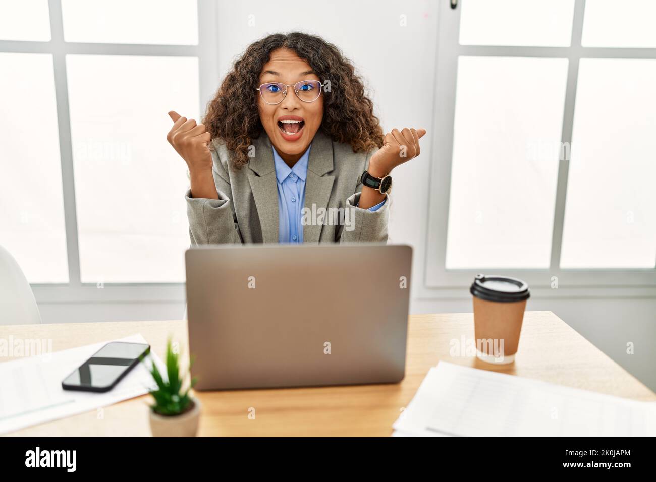 Beautiful hispanic business woman sitting on desk at office working ...