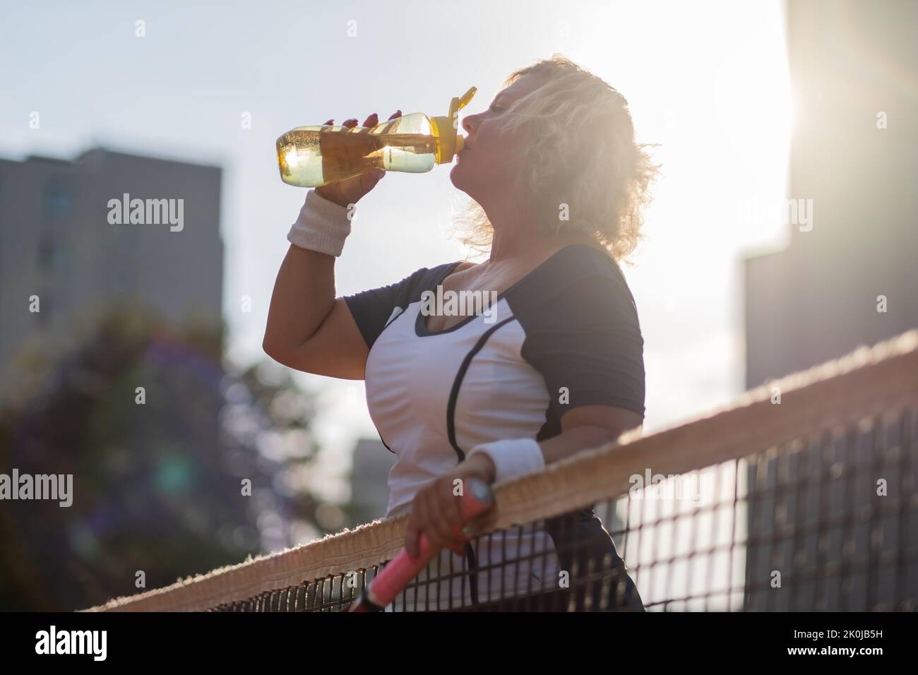 Caucasian mature woman playing tennis and drinking water after game outside. Stock Photo