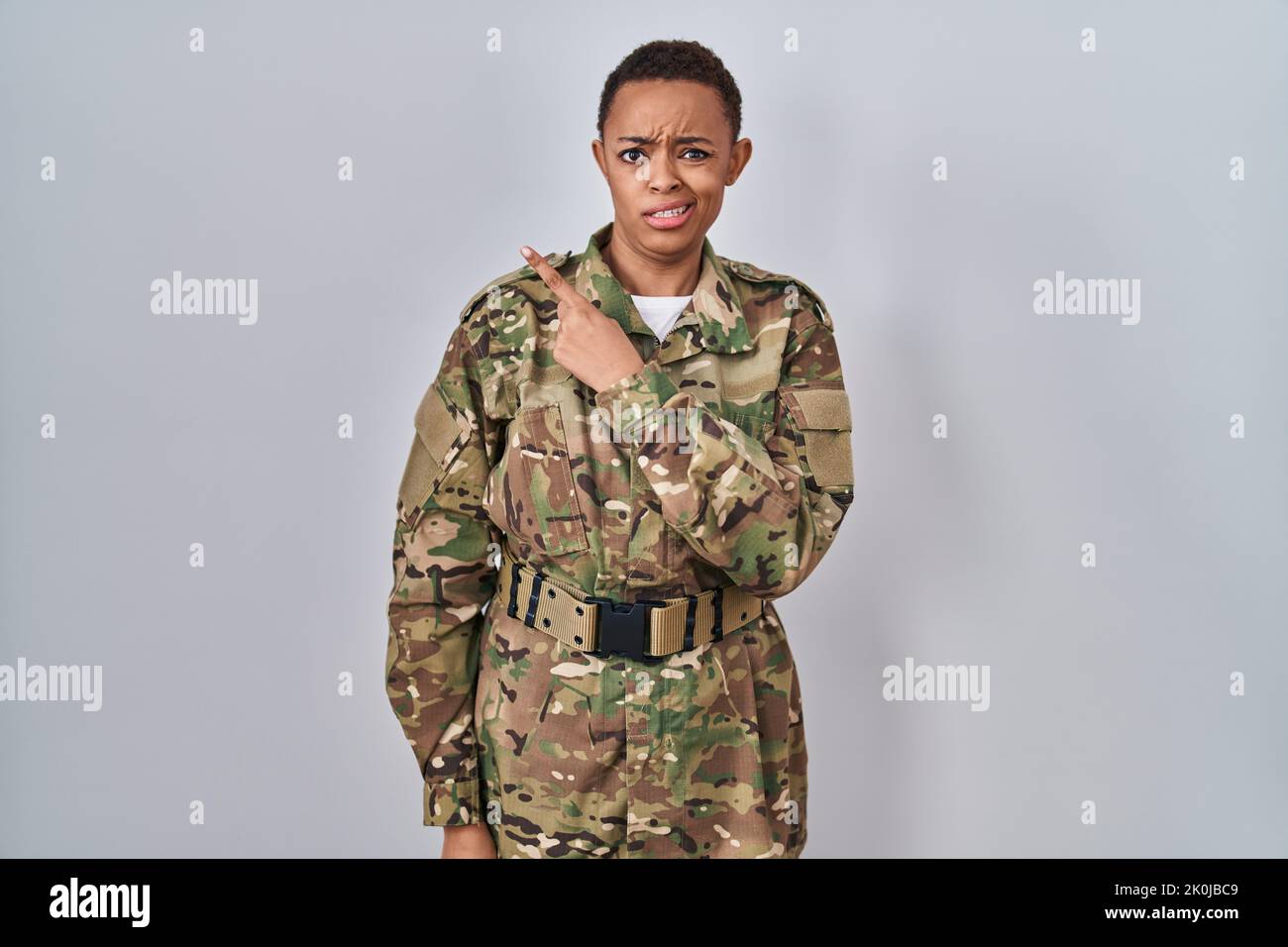 Beautiful african american woman wearing camouflage army uniform pointing aside worried and nervous with forefinger, concerned and surprised expressio Stock Photo