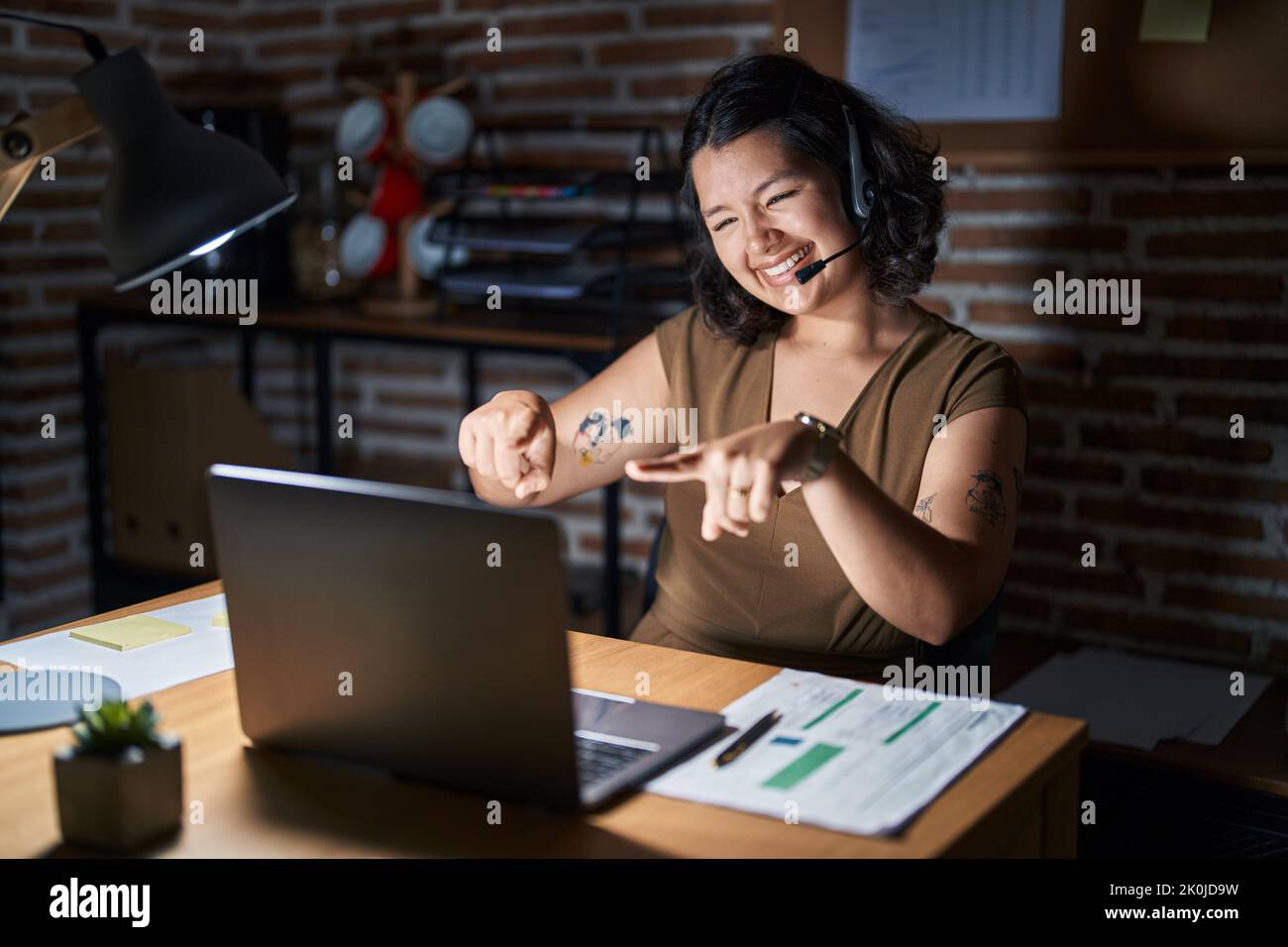 Young hispanic woman working at the office at night pointing to you and ...
