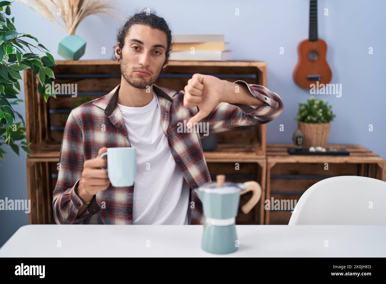 Young hispanic man drinking coffee from french coffee maker with angry ...