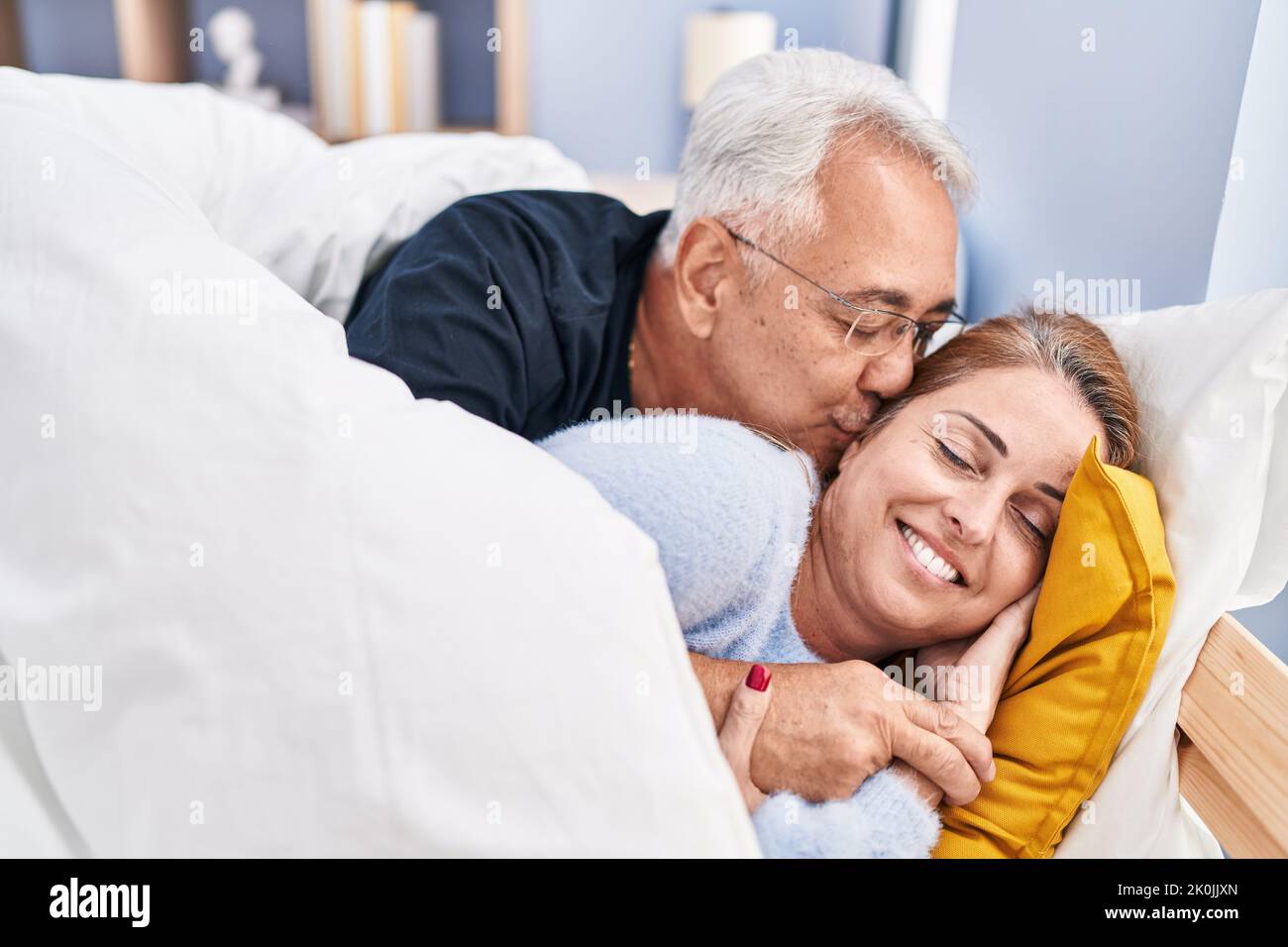 Middle age man and woman couple hugging each other and kissing lying on bed at bedroom Stock