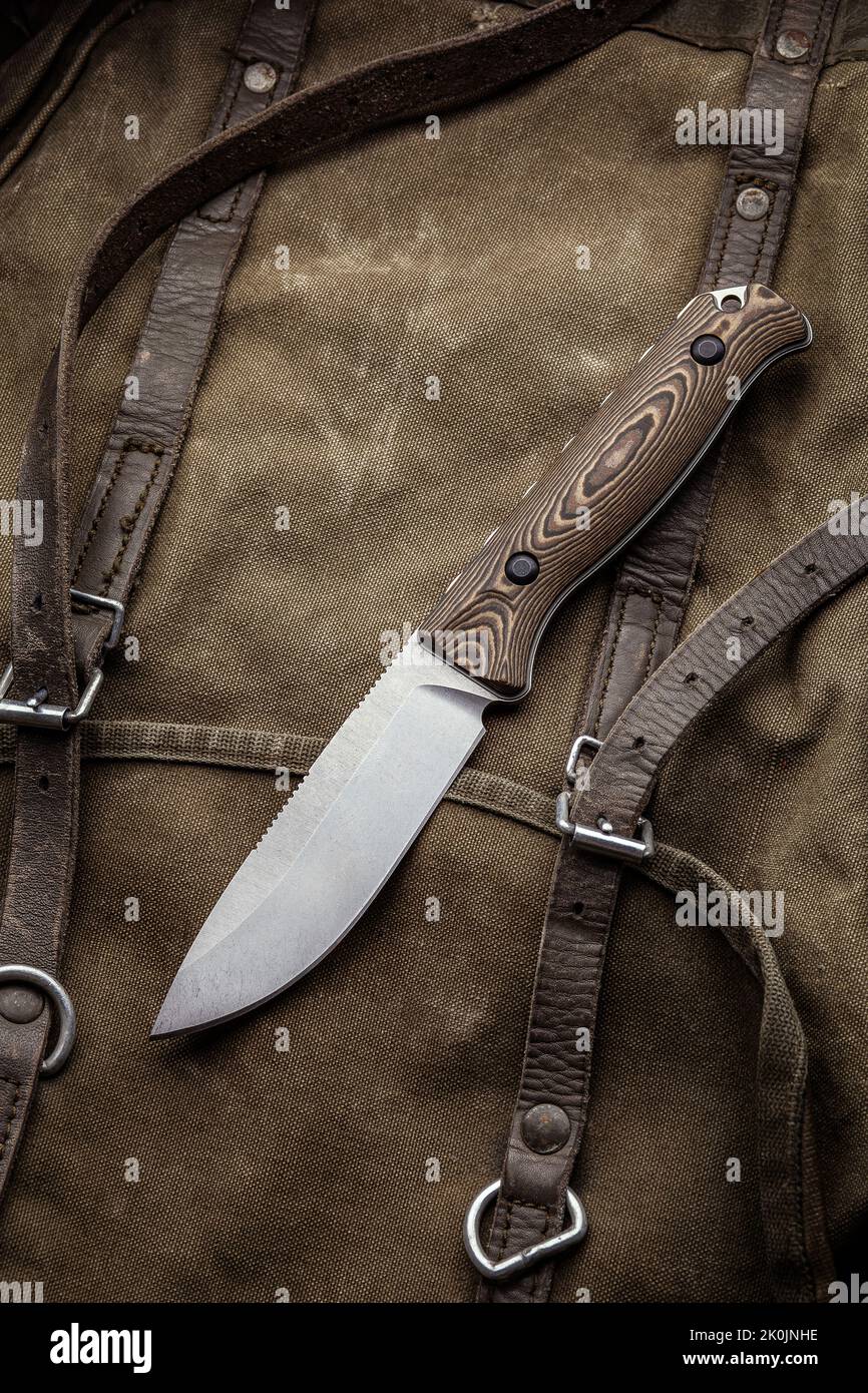 A hunting knife with a wooden handle on a khaki canvas backpack
