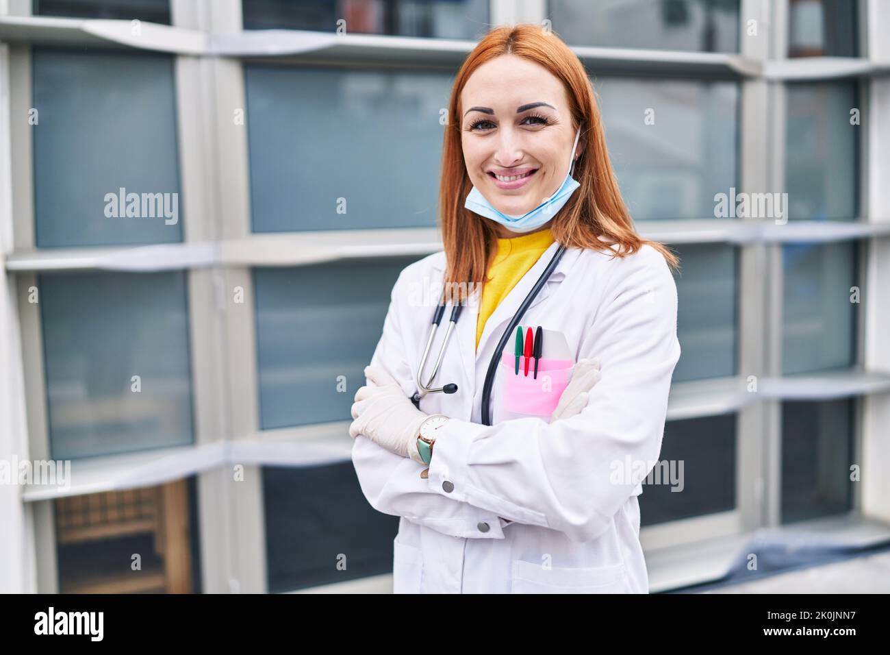 Young caucasian woman doctor wearing medical mask standing with arms ...