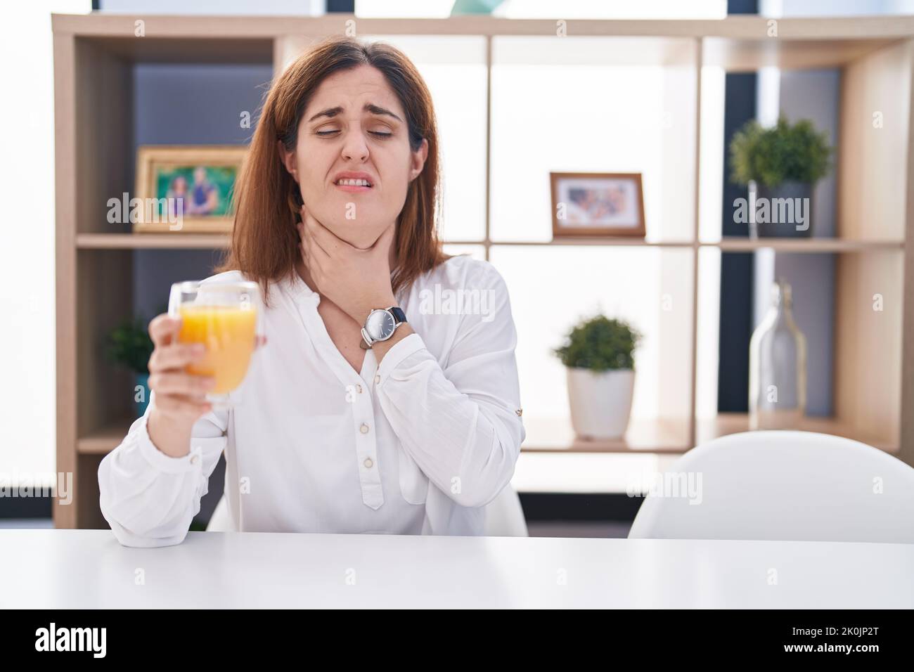 woman drinking glass of orange juice touching painful neck