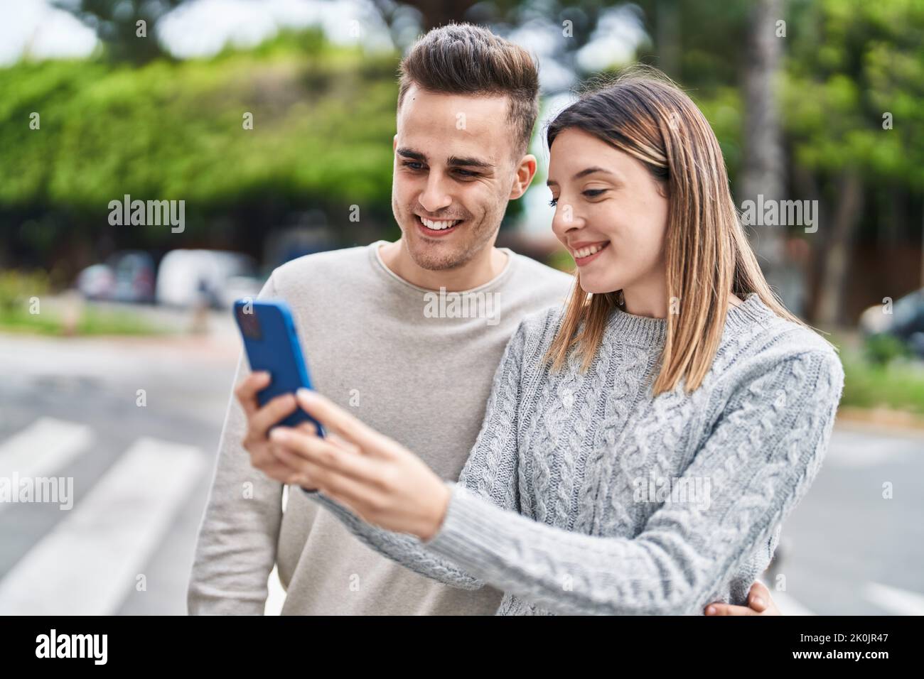 Man and woman couple hugging each other using smartphone at street ...