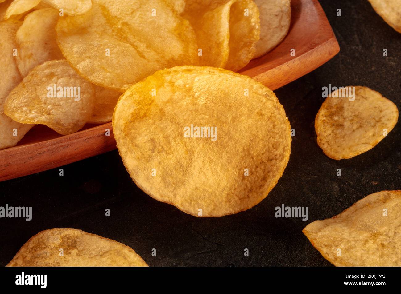 Potato chips or crisps, a salty snack, a close-up on a black slate ...