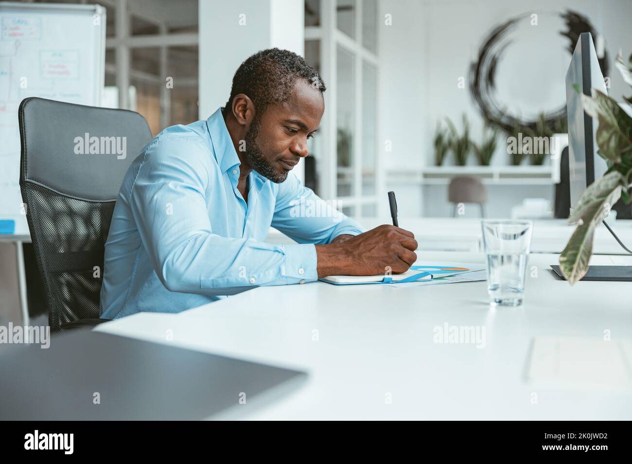 Confident African businessman taking notes while sitting in modern office Stock Photo