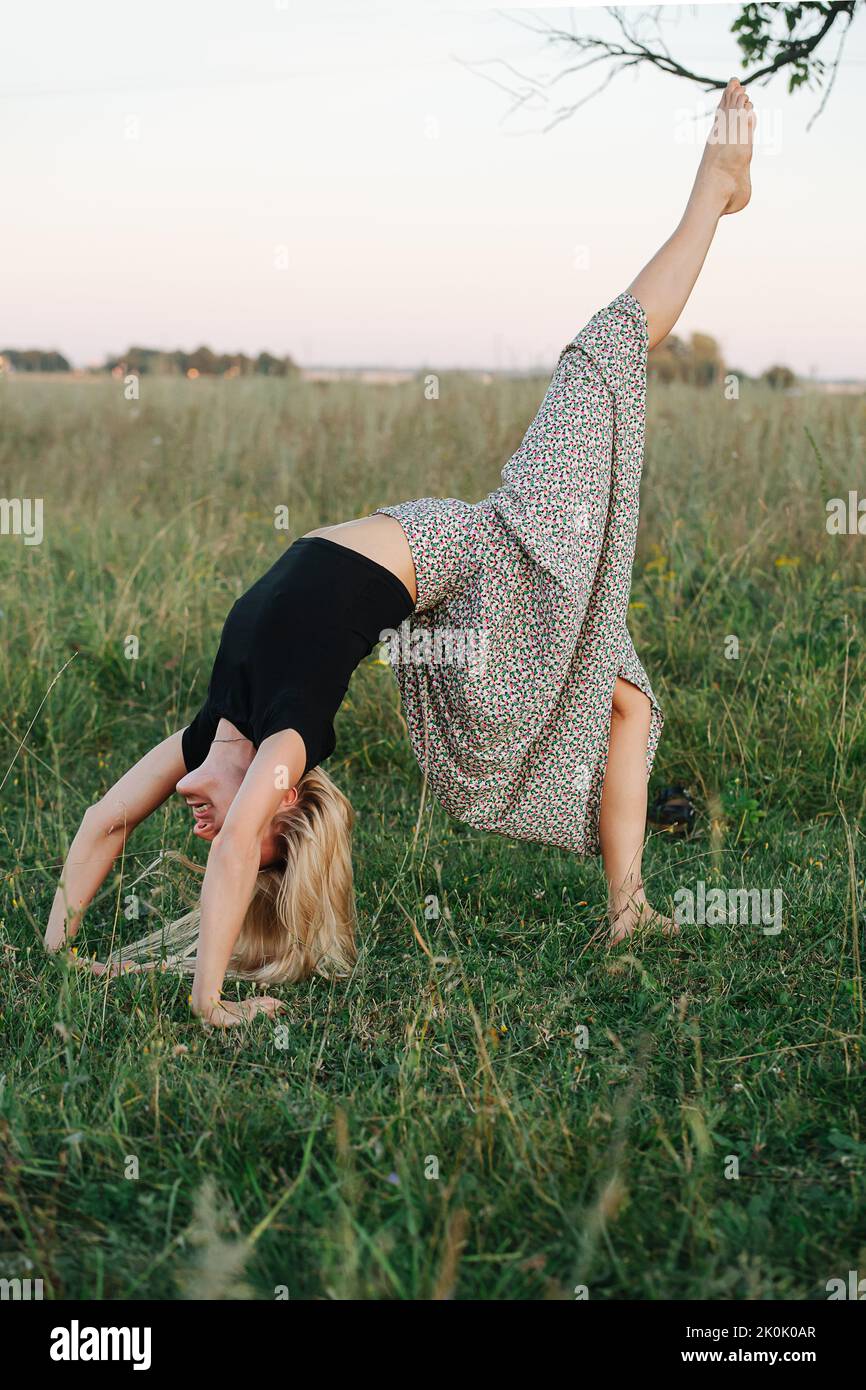 Young blond woman in a field standing in bridge pose with lifted leg Stock Photo