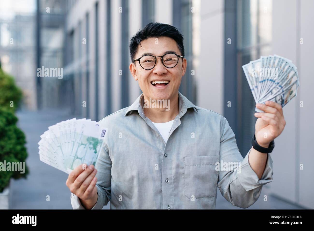 Happy rich asian middle aged man holding two fans of money, celebrating