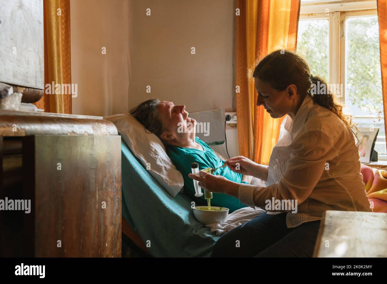 Side view of female nurse feeding paralyzed elderly lady with puree