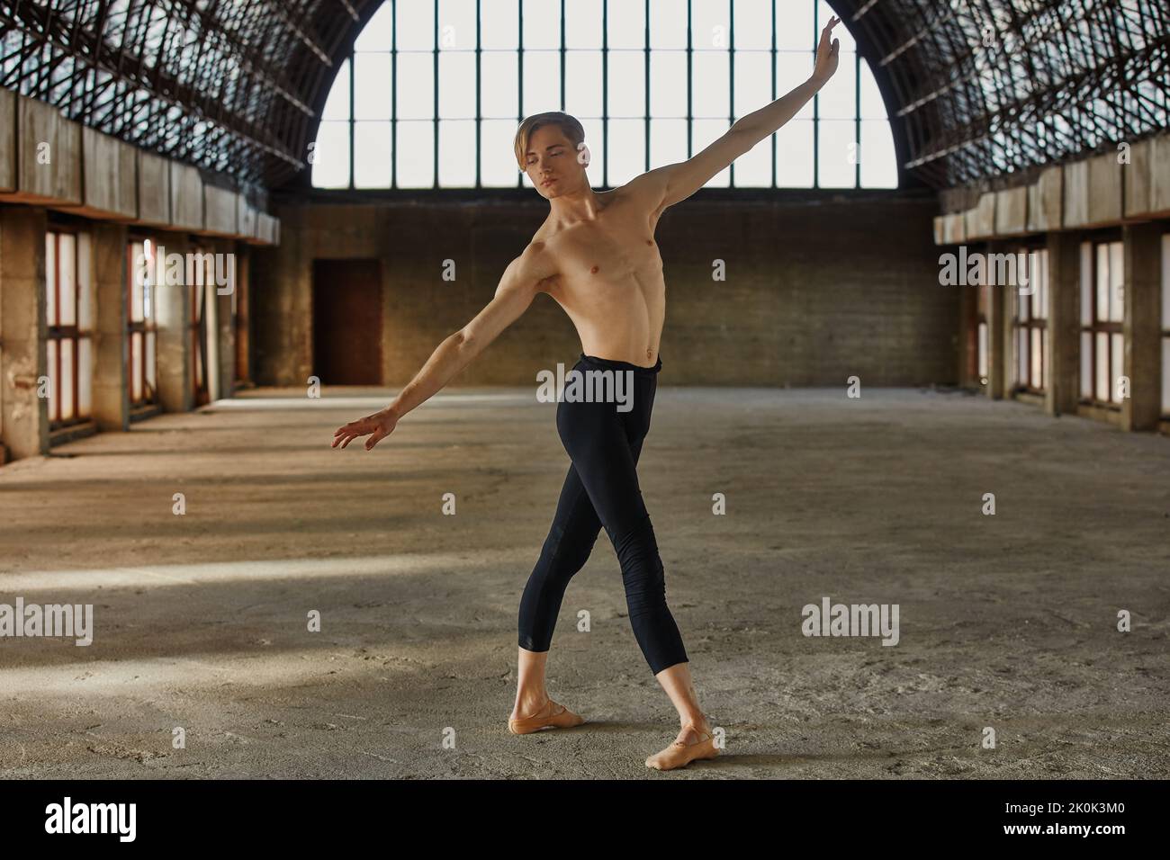 Flexible young ballet dancer in leotard training in large empty hall Stock Photo