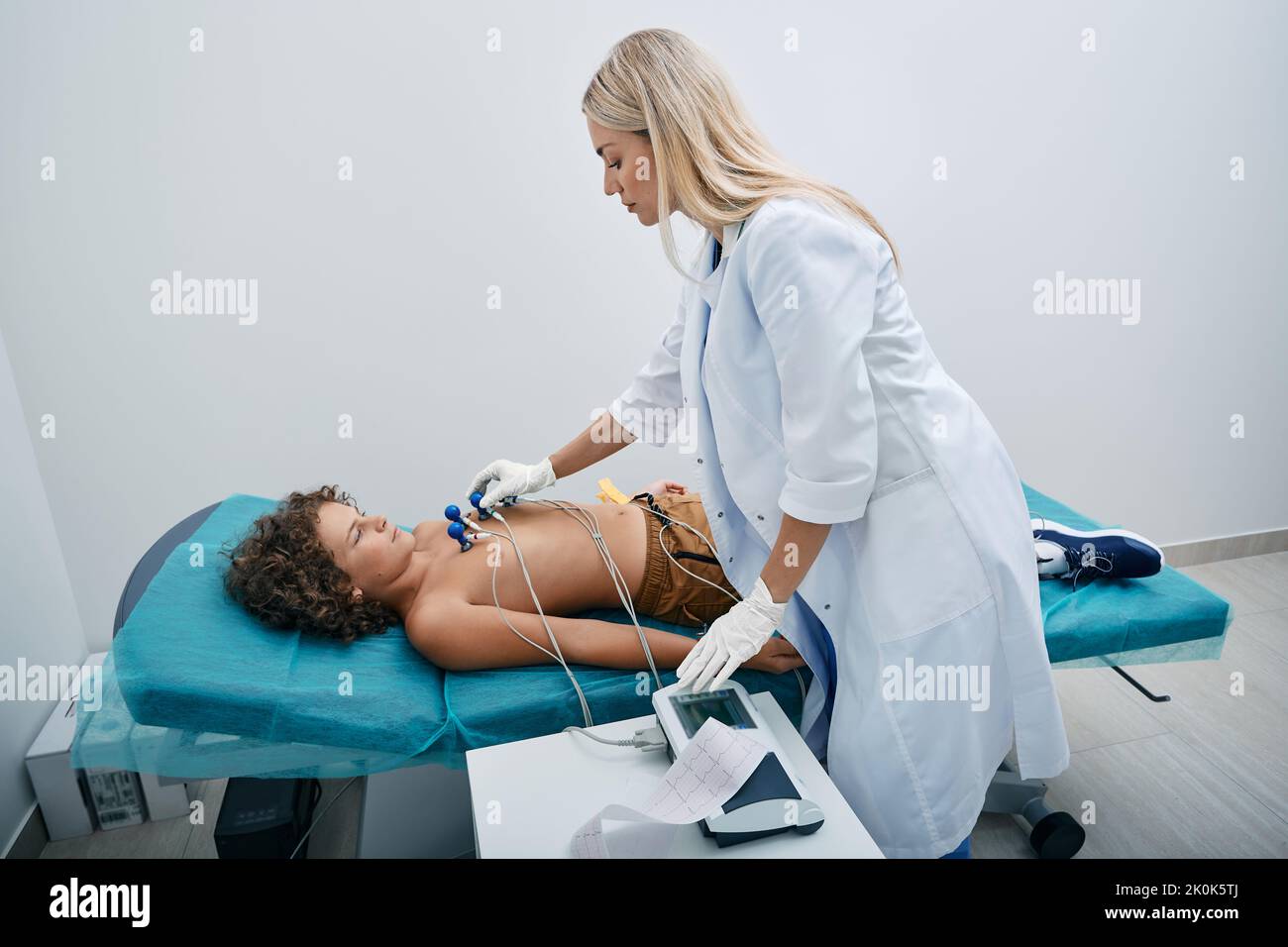 Cardiologist installing vacuum sensors on male child chest during electrocardiogram procedure at medical clinic. ECG for children Stock Photo