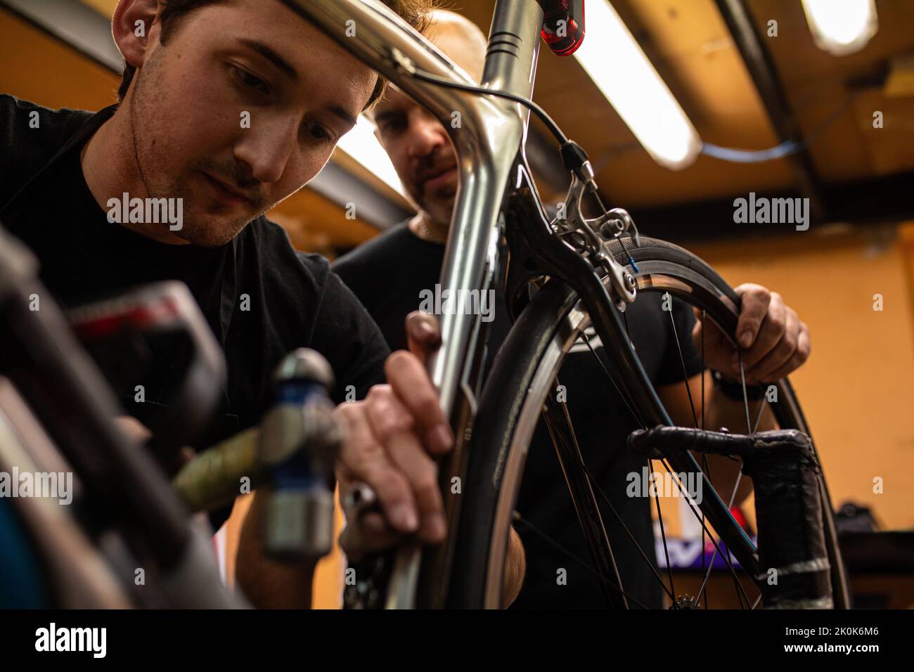 Technician with dirty hands fixing bicycle wheel while working in workshop Stock Photo