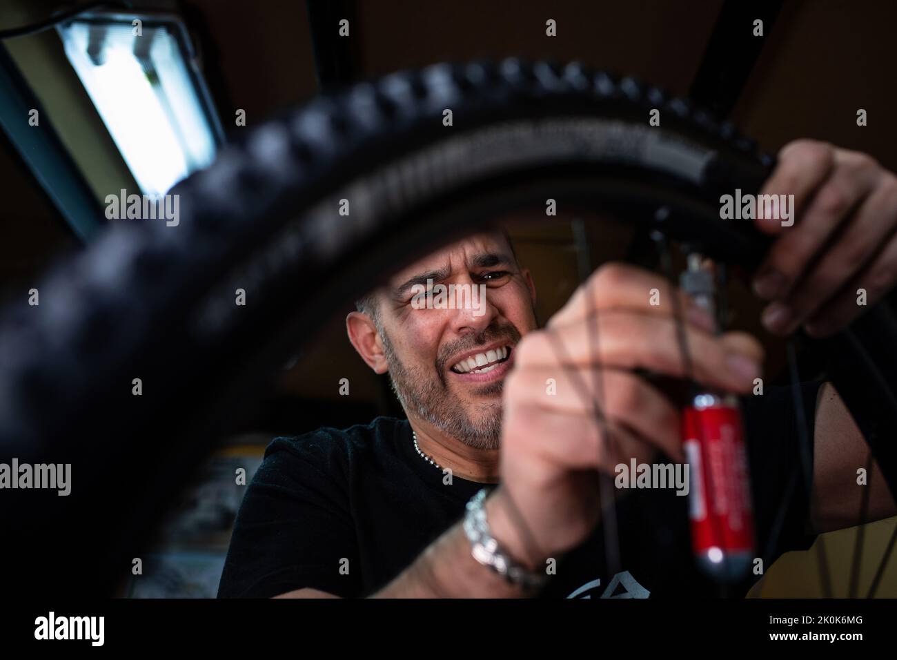 Technician with dirty hands fixing bicycle wheel while working in workshop Stock Photo