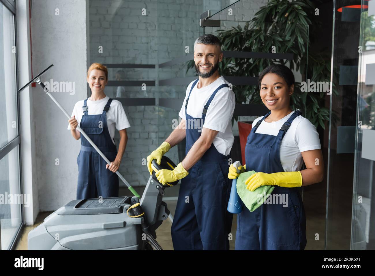 happy interracial team of professional cleaners with cleaning supplies