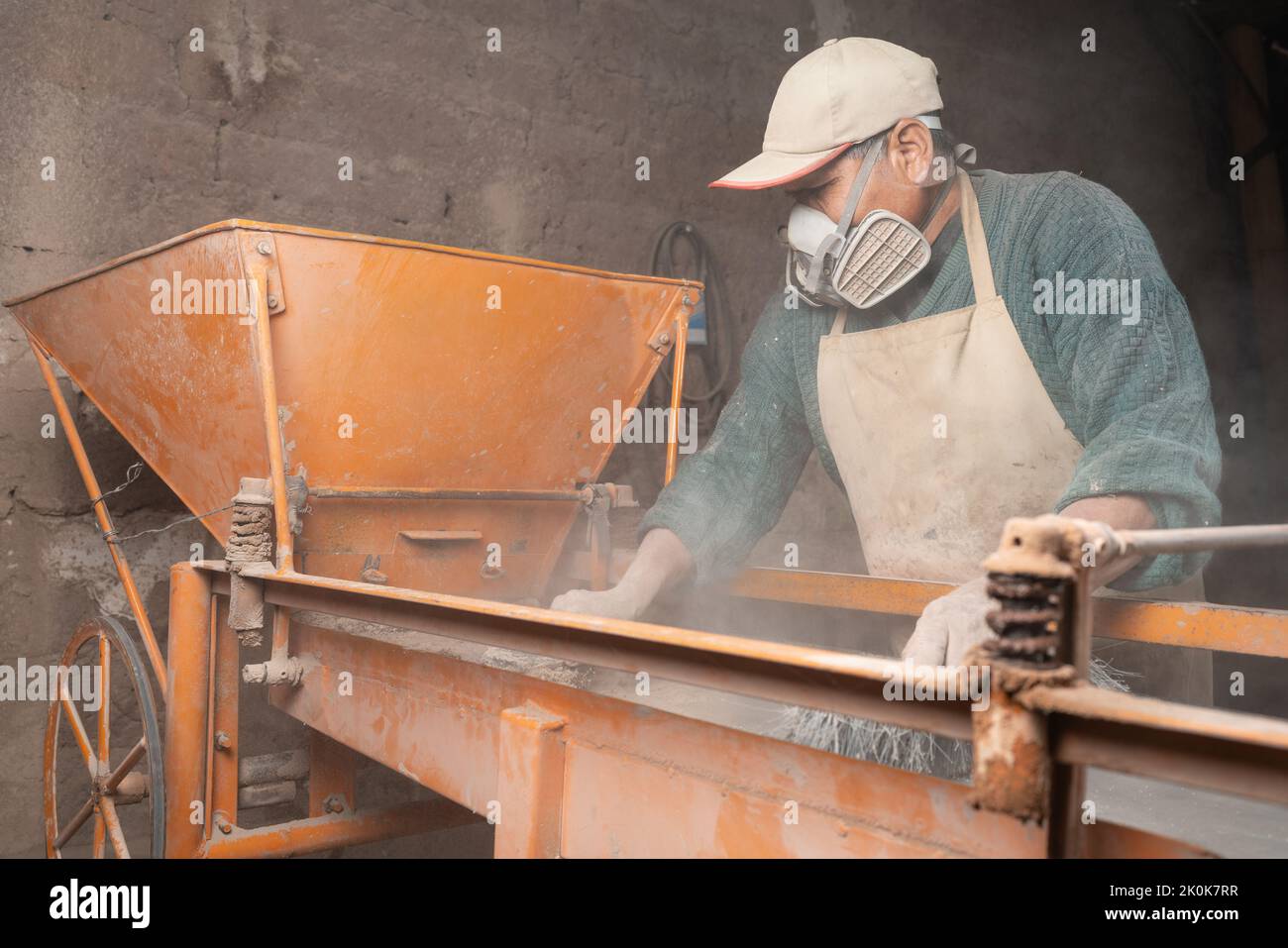 Male worker in apron and protective respirator cleaning plaster station