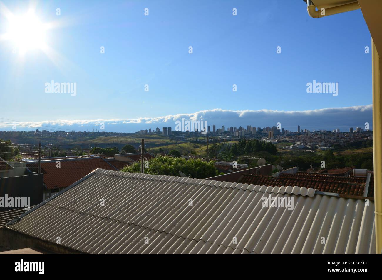 Dusk. Panoramic view of downtown with sun, cold front clouds and house roofs in the foreground, blue sky, wide angle, São Paulo countryside, Brazil, Stock Photo