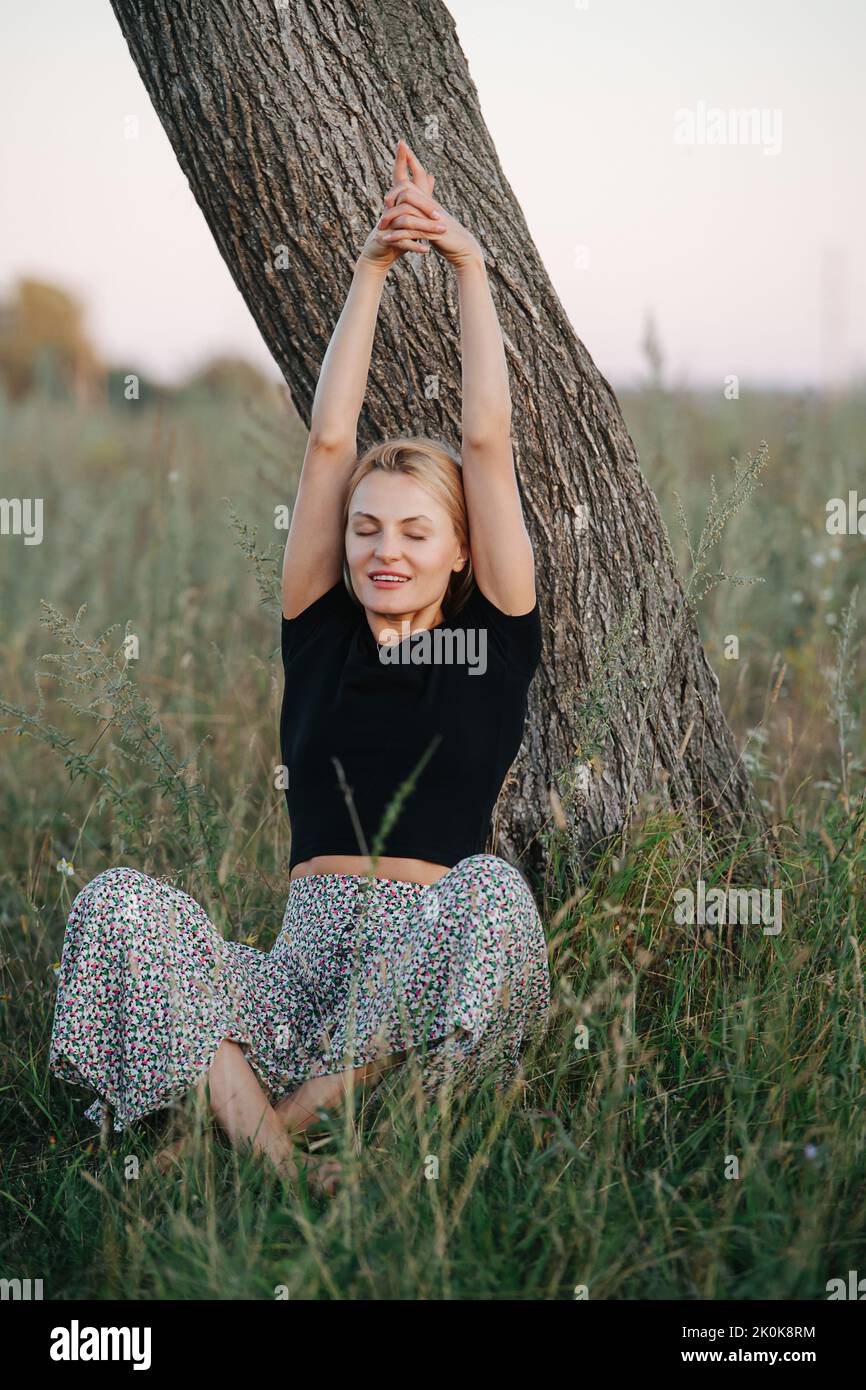 Stretching under a tree blond woman sitting on grass Stock Photo