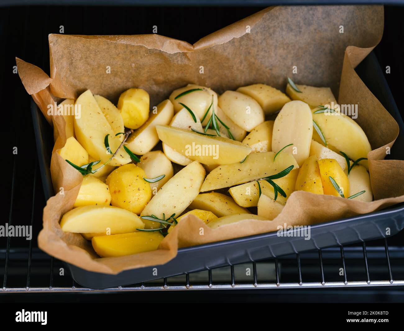 Raw potatoes with rosemary and spices in a black baking tray ready to baked in an oven. Stock Photo