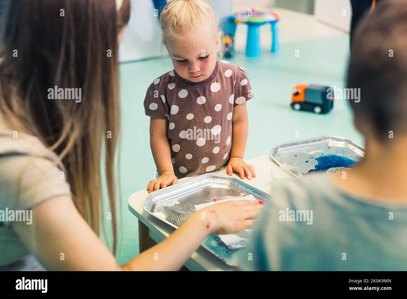 Little caucasian cute girl with other children milk painting, adding food coloring to the milk with a teacher in the classroom at the nursery school. High quality photo Stock Photo