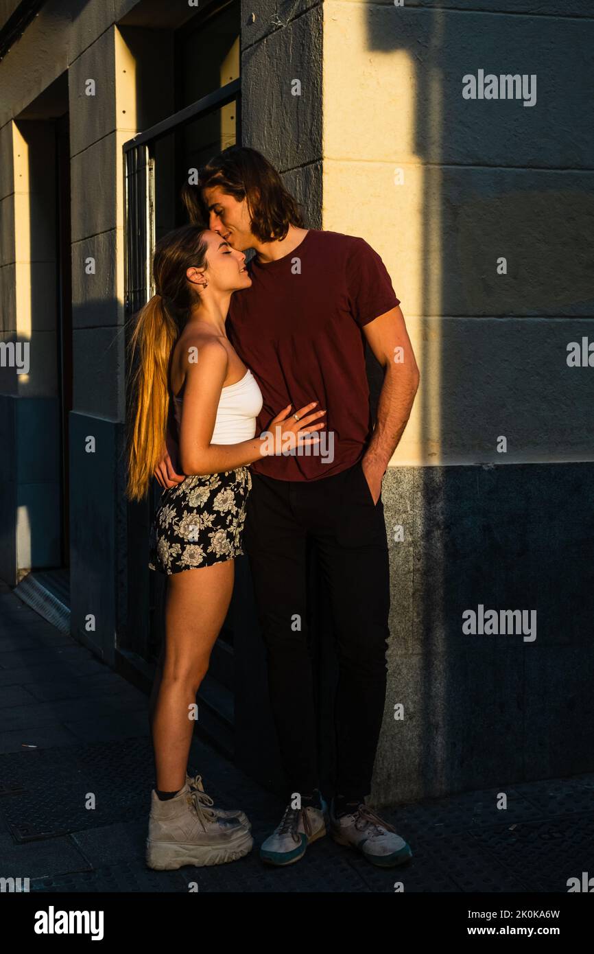 Full body of young loving man and woman in casual clothes cuddling standing  on street near modern gray building and kissing other during sunset time  Stock Photo - Alamy