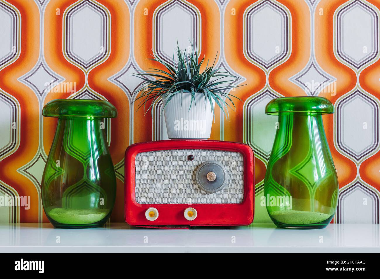 Retro fashioned radio and plant in flowerpot placed on table between green glass jars against colorful wall Stock Photo