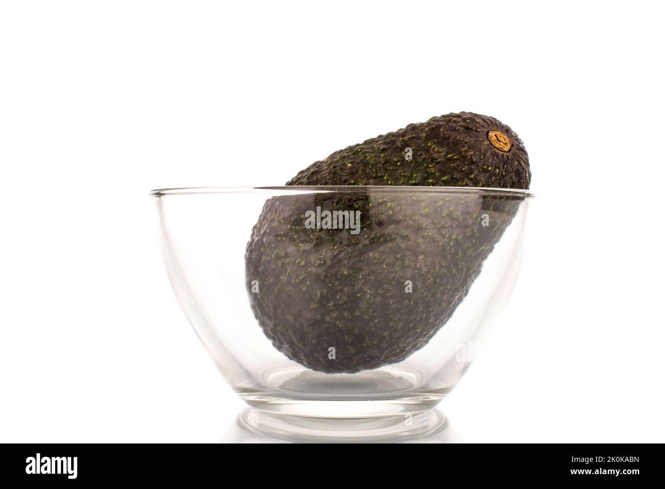 One ripe organic avocado in a glass bowl, close-up, isolated on a white background. Stock Photo
