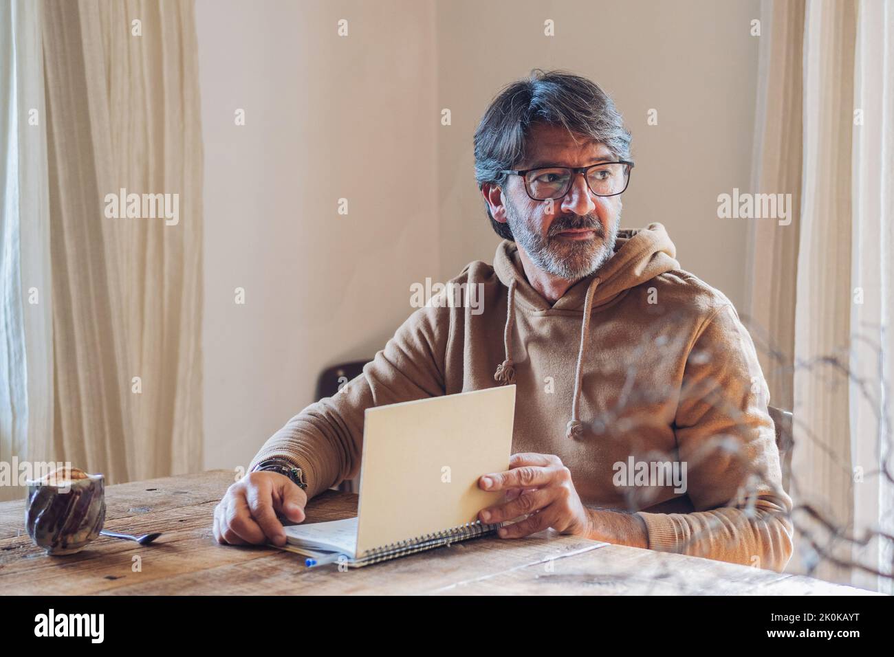 Side view of focused aged bearded male writing in notebook while ...