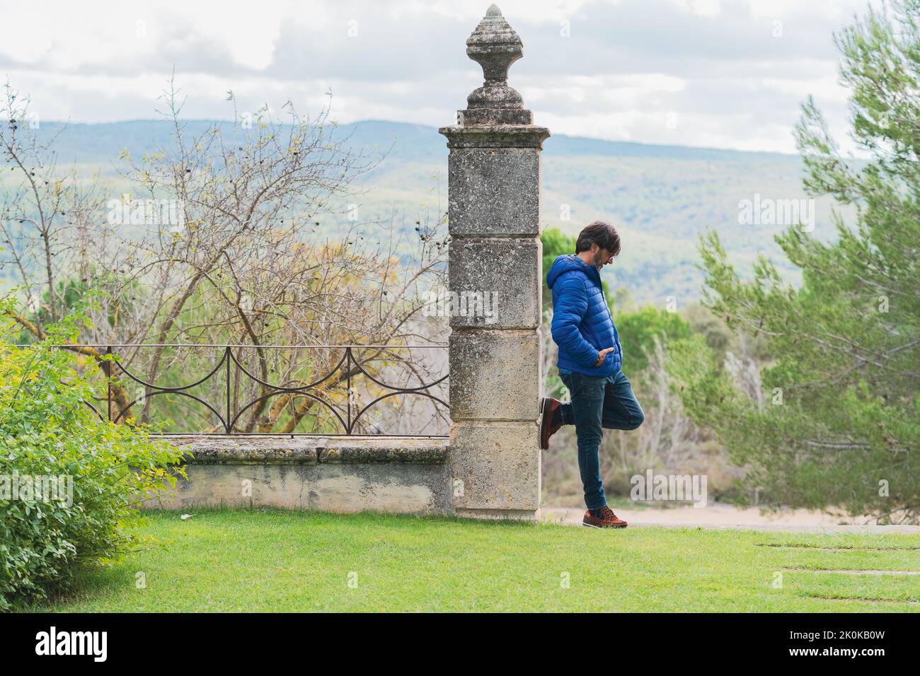 Middle-aged man leaning on a stone column while pensively looking at the sky Stock Photo