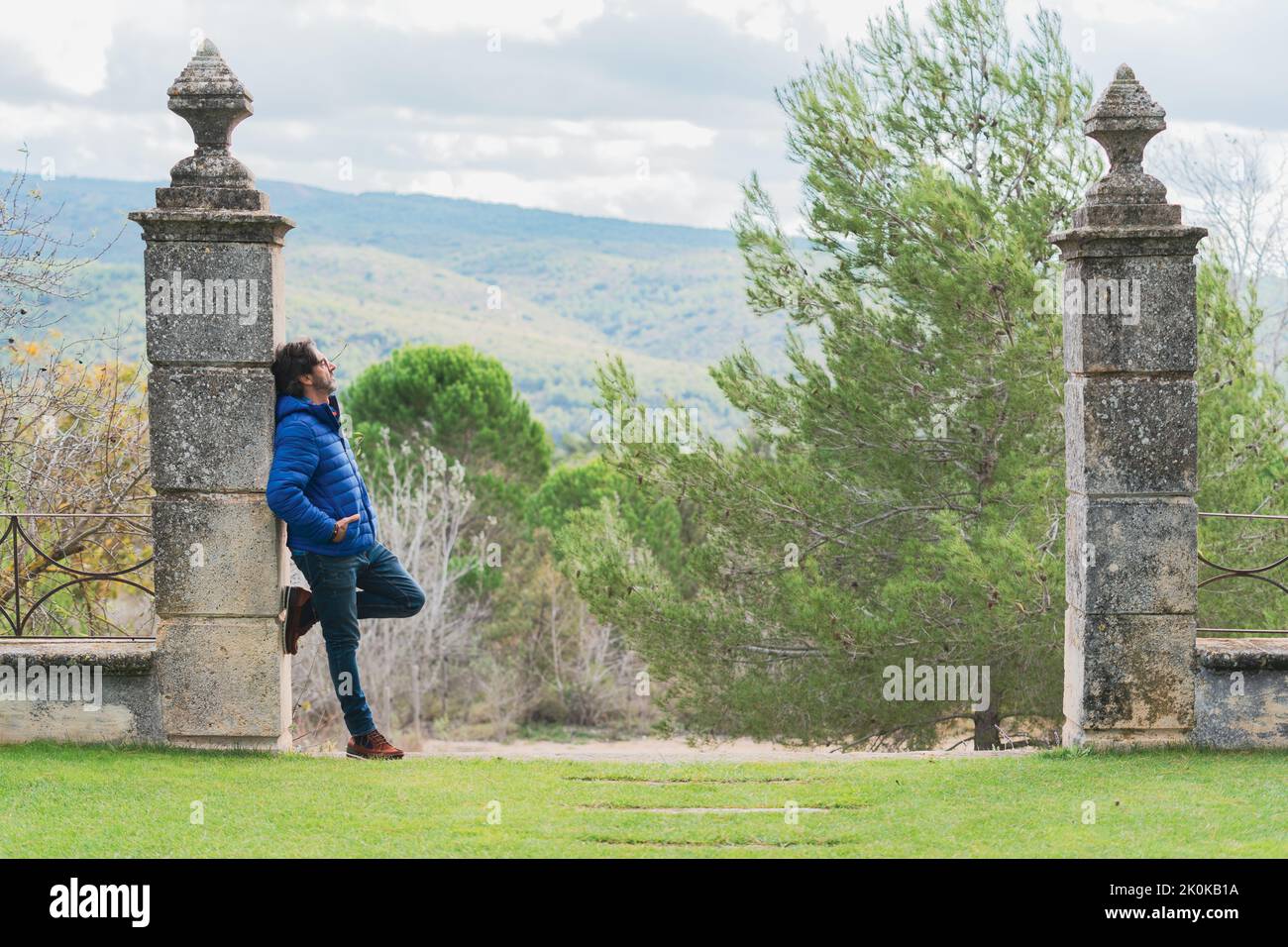 Middle-aged man leaning on a stone column while pensively looking at the sky Stock Photo