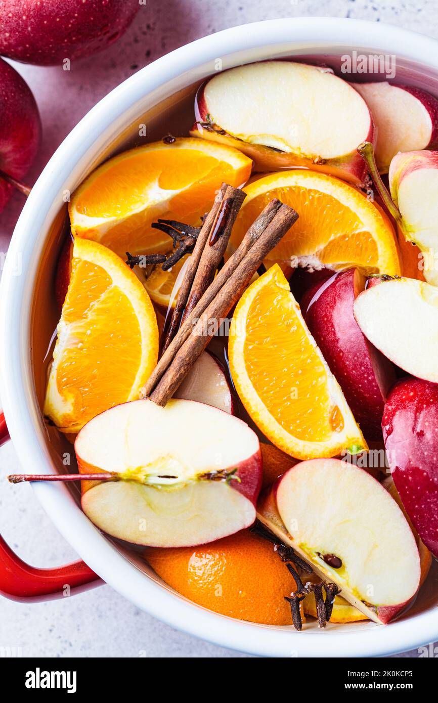 Cooking homemade hot cider from apples and oranges with spices in a red saucepan, top view. Autumn or winter warming drink. Stock Photo