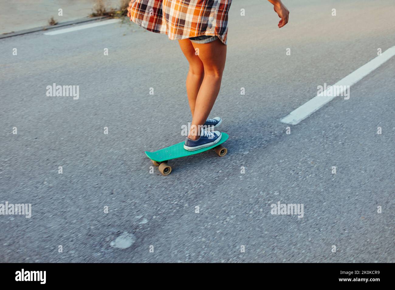 Crop of Back view of female hipster riding penny board along empty road ...