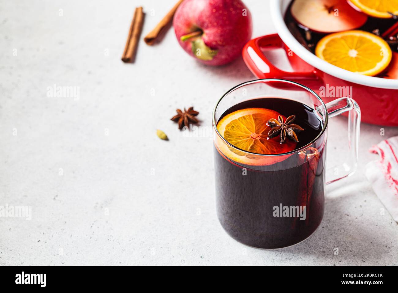 Mulled wine with orange, apple and spices in a glass mug, gray background, copy space. Autumn or winter cozy drink. Stock Photo