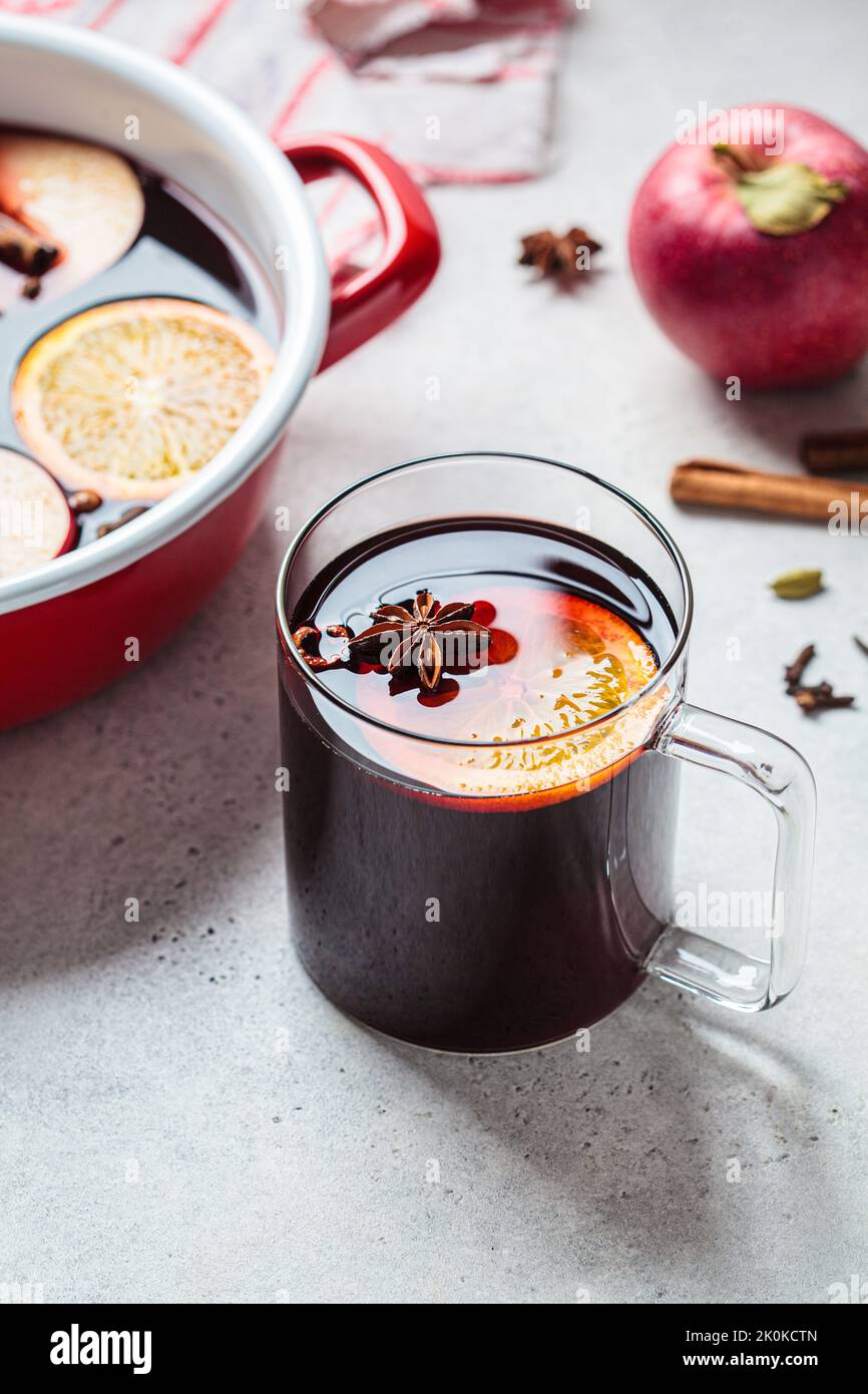 Mulled wine with orange, apple and spices in a glass mug, gray background. Autumn or winter cozy drink. Stock Photo
