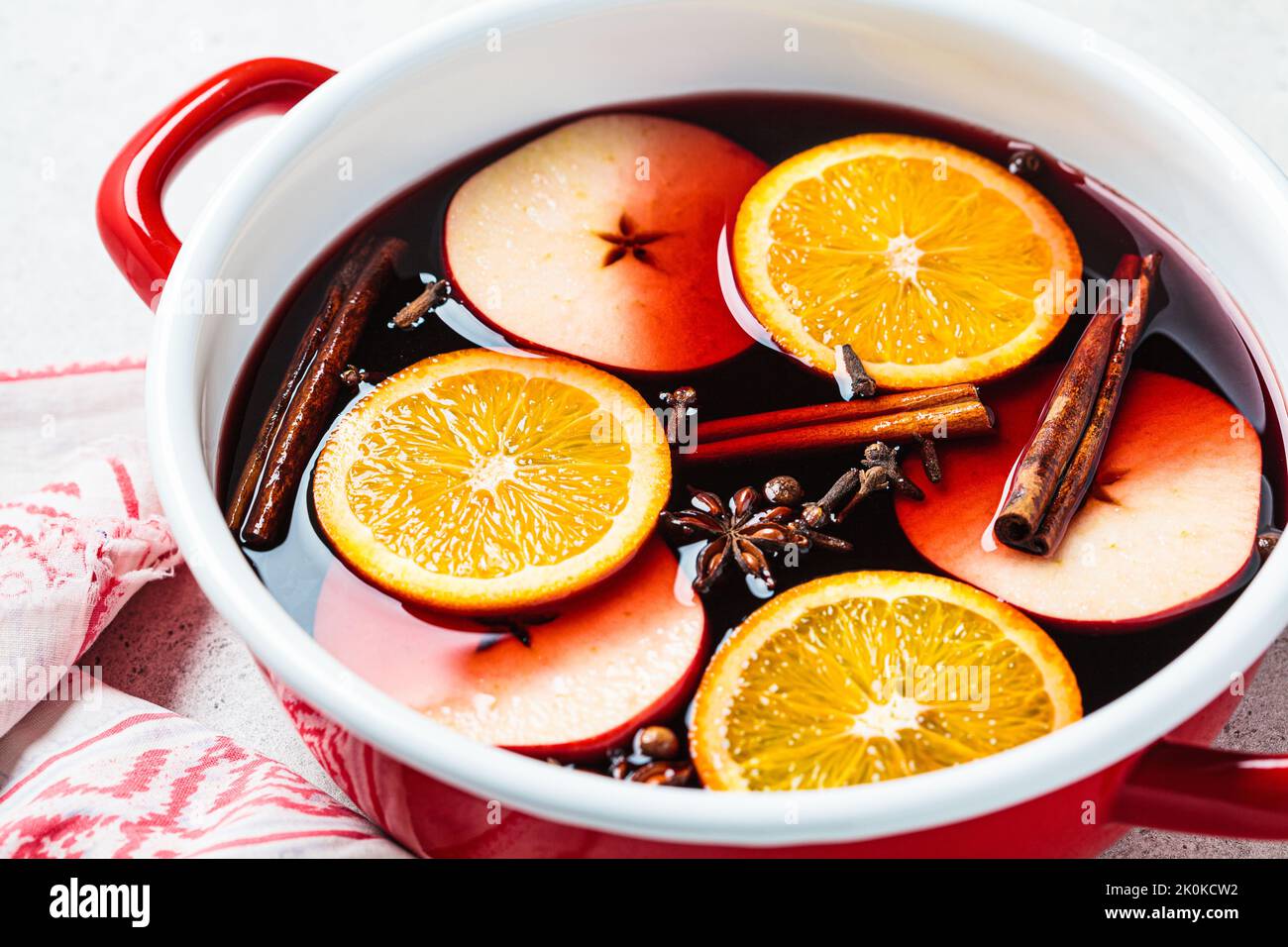 Mulled wine with orange, apple and spices in a red saucepan, gray background. Autumn or winter cozy drink. Stock Photo
