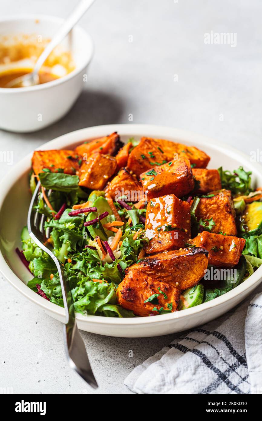 Baked sweet potato and green salad bowl with mustard dressing. Vegan food concept. Stock Photo