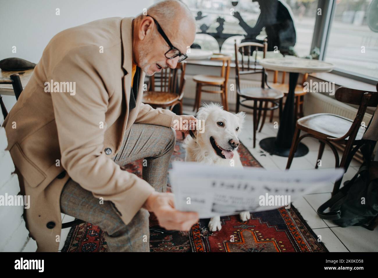 Happy senior man sitting in cafeteria and reading newspaper with his dog. Stock Photo