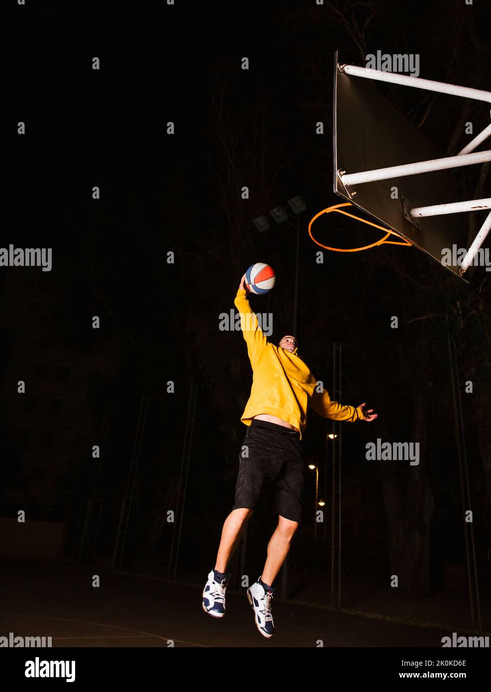 Basketball player in yellow sport clothes jumping and making dunk while training on sports