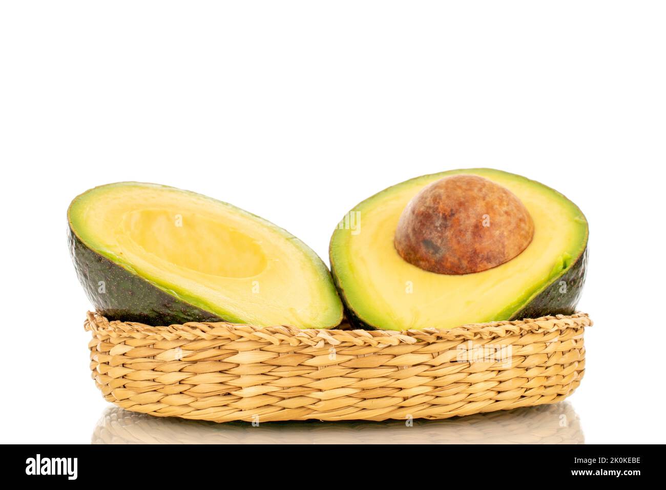 Two halves of a ripe organic avocado in a straw bowl, close-up, isolated on a white background. Stock Photo