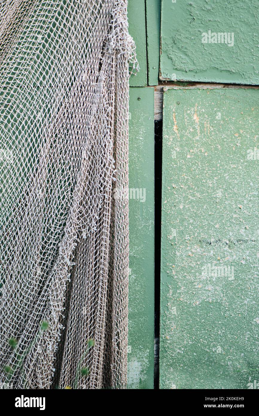 Fishing net hanging on a green painted plywood wall of a shack Stock Photo