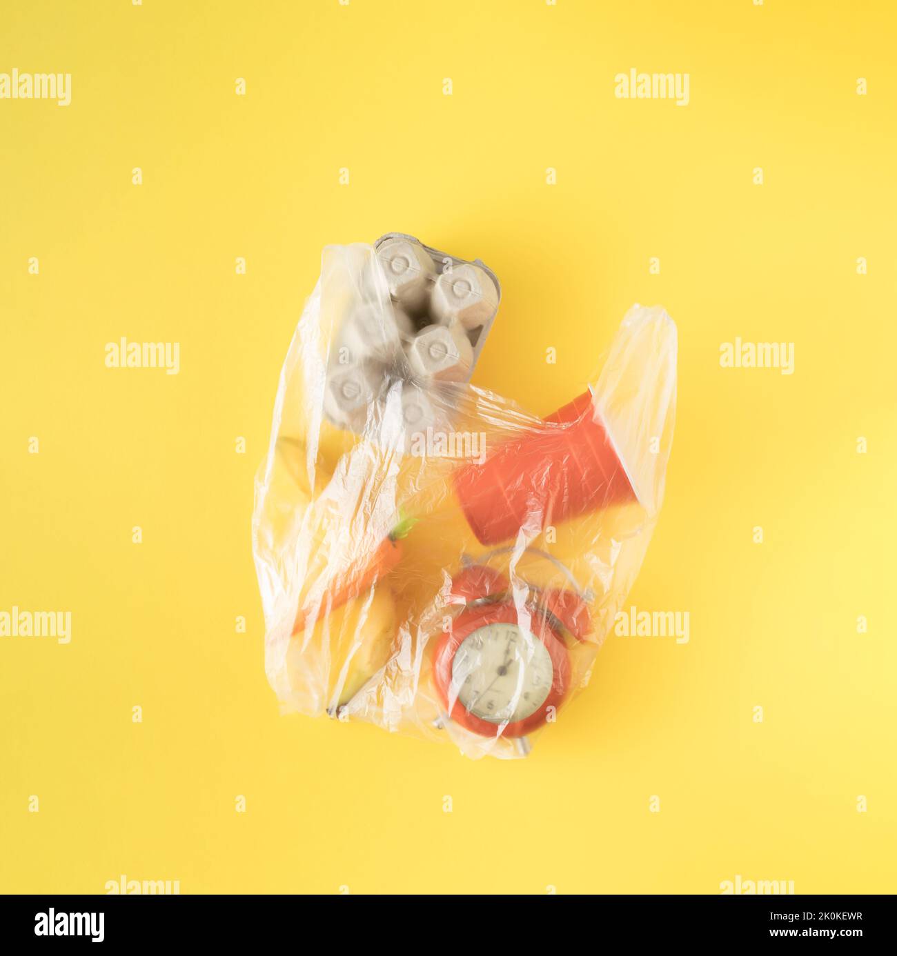 Plastic transparent bag with cardboard egg box, carrot, banana, clock
