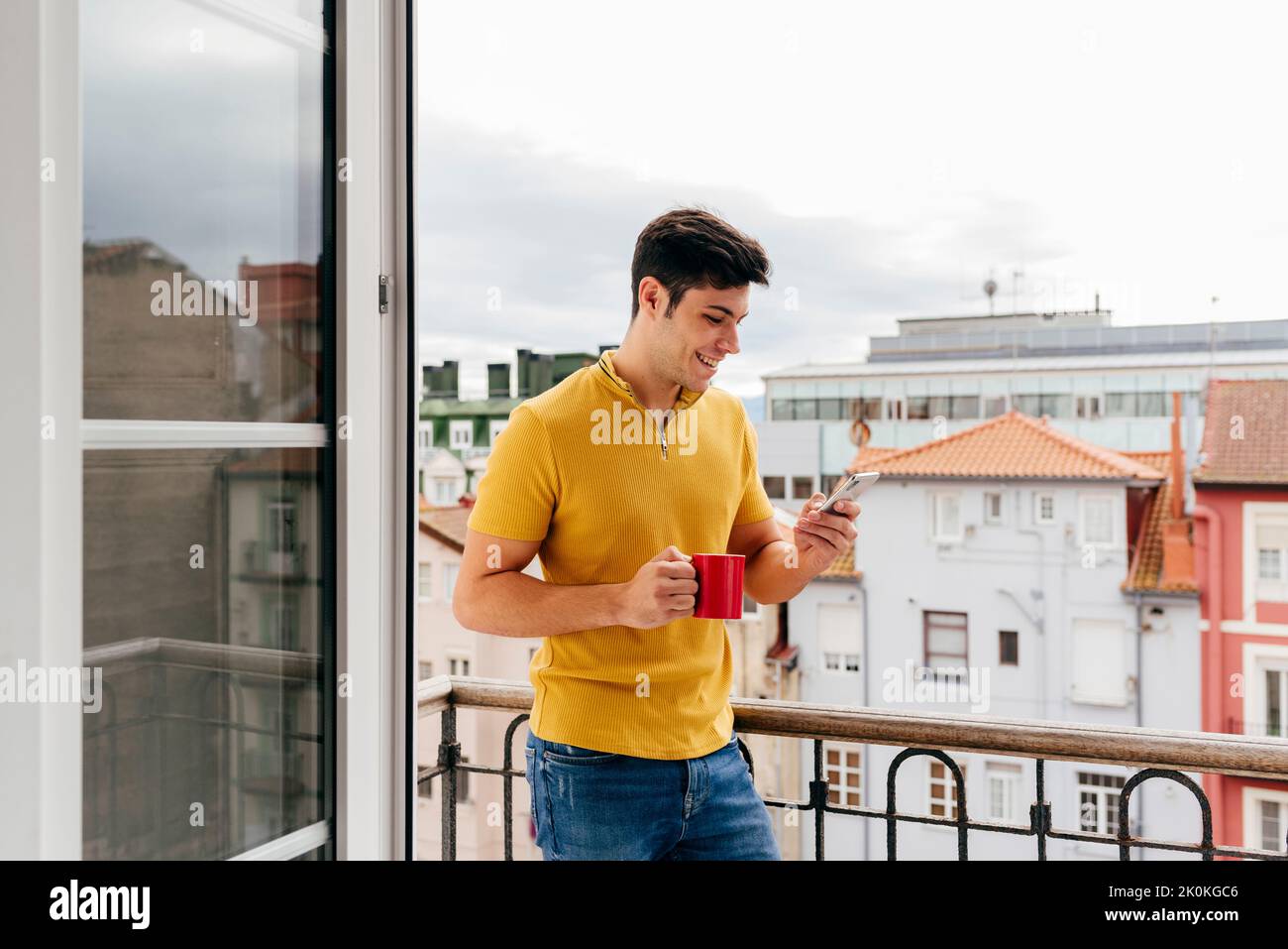 Attractive caucasian man with a coffee cup on the balcony at home using mobile phone Stock Photo